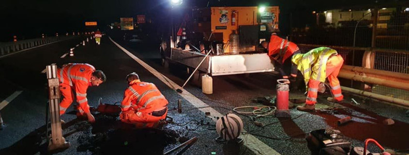 Lavoratori in un cantiere stradale notturno con DPI ad alta visibilità e illuminazione di sicurezza